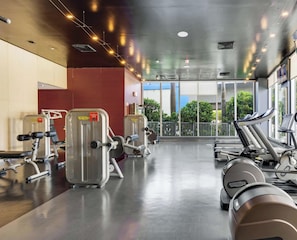 Ein Fitnessraum mit Cardiogeräten, Gewichten und großen Fenstern mit Blick ins Freie.