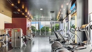Une salle de sport équipée de machines de cardio, de machines de musculation et dotée d’une grande fenêtre donnant sur un espace verdoyant.