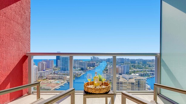 A balcony with a city view, a table with a basket of snacks, and a bottle of liquor. - Modern Spacious Studio - Resort‑Style Experience (Hallandale Beach)