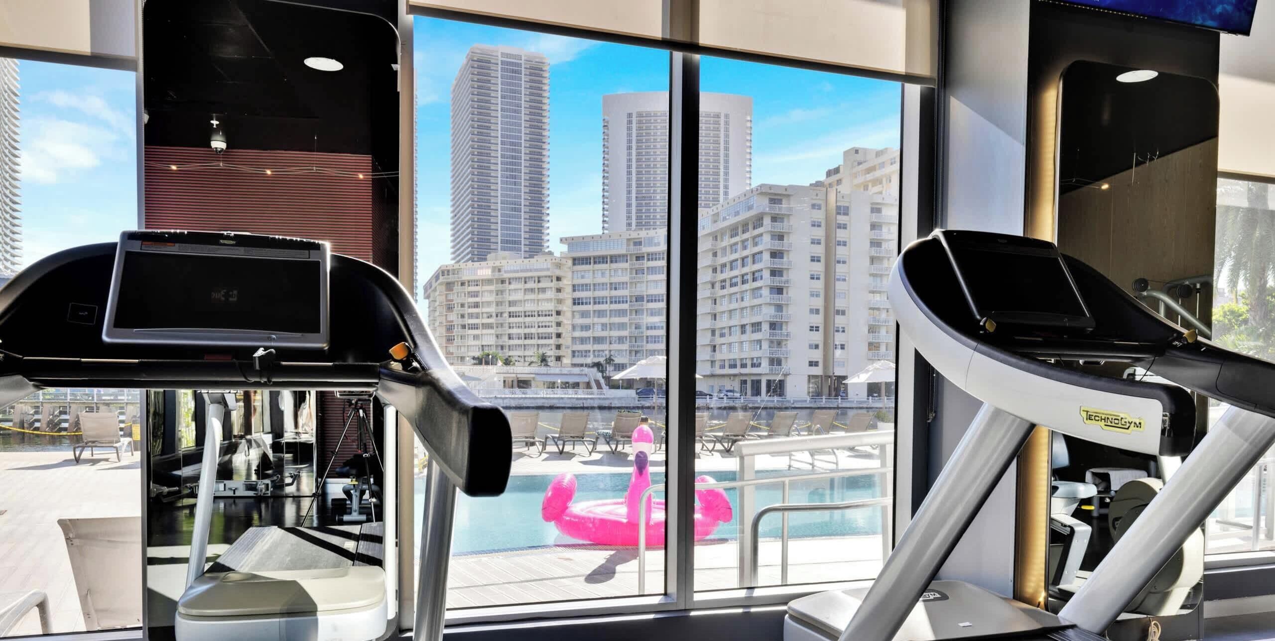 A gym with exercise equipment and a view of a cityscape through large windows.