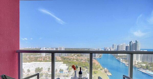 Un balcón con vistas despejadas a un río, un paisaje urbano y un florero con una flor.