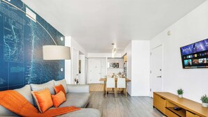 Un salon moderne avec une grande carte accrochée au mur, un canapé gris agrémenté de coussins orange et une table à manger en bois avec des chaises.