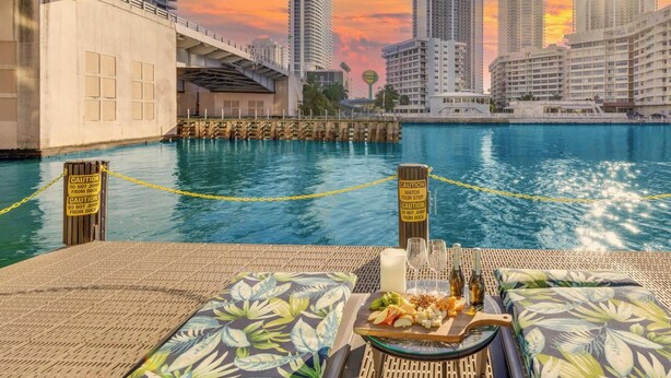 Un espace de restauration situé au bord de l’eau, offrant une vue sur les gratte-ciel de la ville, un quai et des panneaux d’avertissement.