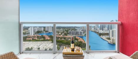 A balcony with wicker furniture, a bottle of wine, and glasses on a tray.