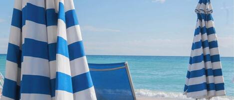 Una spiaggia con due ombrelloni a righe e una sedia a sdraio blu.