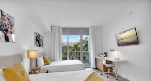 A hotel room with two beds, a desk, a chair, a TV, and a balcony with a view. - Hallandale Studio | Sunset Pool (Hallandale Beach)