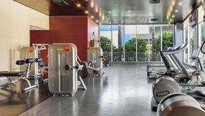 A gym with cardio machines, weight machines, and a large window with a view of greenery. - Cozy Studio with Private Balcony & Bay View (Hallandale Beach)