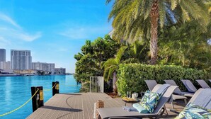 A waterfront lounge area with lounge chairs, a pool, and a city skyline in the background. - Cozy Studio with Private Balcony & Bay View (Hallandale Beach)