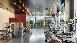 A gym with cardio machines, weight training equipment, and a large window providing a view of the outdoors. - Bright Studio | Intracoastal View & Pool (Hallandale Beach)