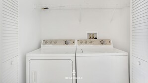Une machine à laver et un sèche-linge à chargement frontal, tous deux de couleur blanche, se trouvent dans une buanderie, avec un étendoir en métal placé au-dessus.