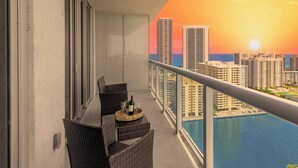 Un balcón con vista al horizonte de una ciudad al atardecer, una mesa de comedor con sillas y una piscina.