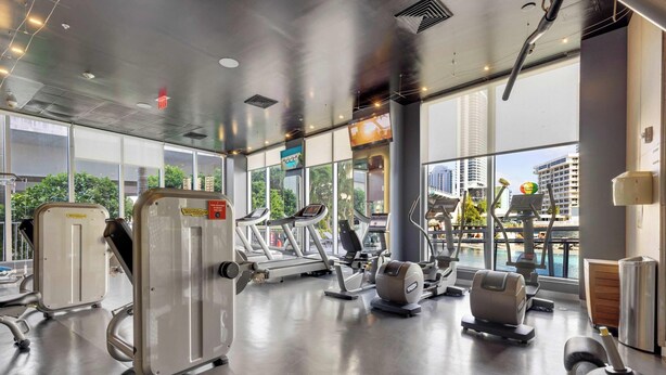 Un gimnasio con máquinas de cardio, zonas de pesas y un amplio ventanal con vistas a la ciudad.