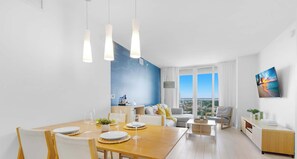 A modern living room with a dining area, large windows, and a city view. - New! 1BR Intracoastal & Marina View, Pool & Beach (Hallandale Beach)