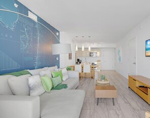 A modern living room with a large map on the wall, a dining area, and a kitchen in the background. - Sunset View Apt | Full Kitchen & Beach Shuttle (Hallandale Beach)