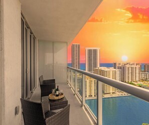 A balcony with wicker chairs, a table, and a bottle of wine. - Sunset View Apt | Full Kitchen & Beach Shuttle (Hallandale Beach)