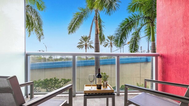 Ein Balkon mit Blick auf Palmen und eine blaue Schutzvorrichtung, ausgestattet mit zwei Stühlen und einem kleinen Tisch.