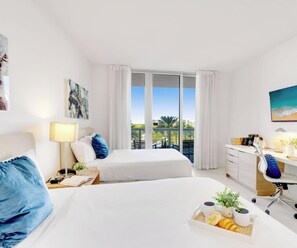 Ein Hotelzimmer mit zwei Betten, einem Schreibtisch, einem Sessel, einem Fernseher und einem Balkon mit Aussicht.