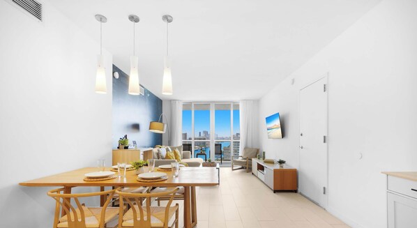 A modern interior with a dining area, kitchen, and living space, featuring a city view through large windows. - High-Floor Balcony · 2BR Resort Sunset View (Hallandale Beach)