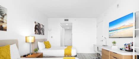 Une chambre d’hôtel avec deux lits, un bureau, une télévision et une salle de bain visible à travers une porte ouverte.