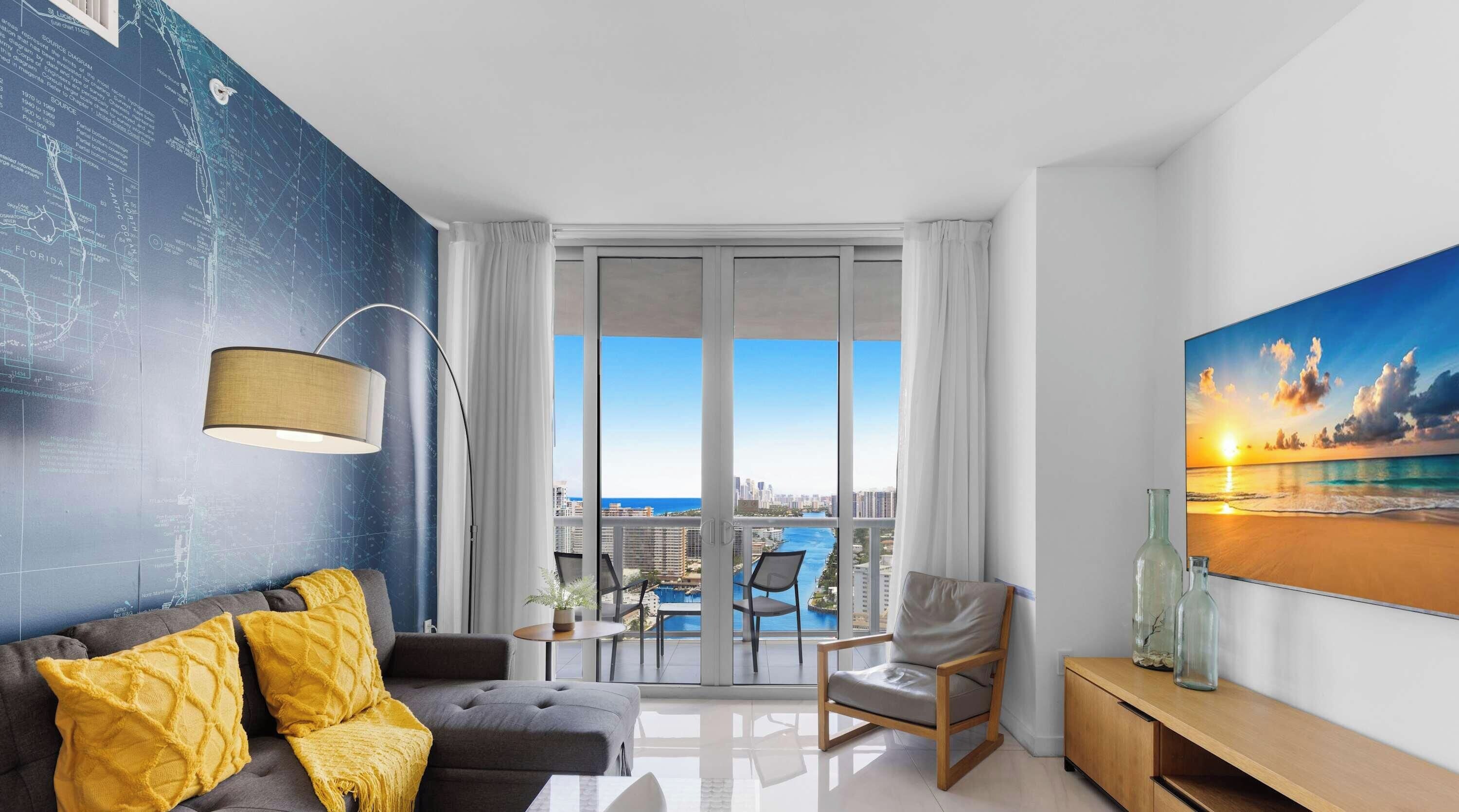 A modern living room with a city view, a large window, and a painting of a sunset.