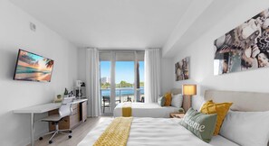 A hotel room with a bed, a desk, a chair, a lamp, and artwork on the walls. - Stylish Studio Near the Beach | Resort Life (Hallandale Beach)