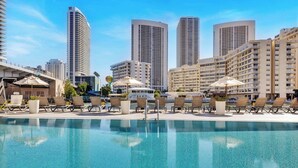 A poolside area with lounge chairs and umbrellas, surrounded by high-rise buildings. - Stylish Studio Near the Beach | Resort Life (Hallandale Beach)