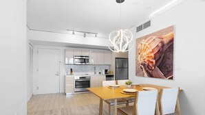 Una cocina moderna con muebles blancos, un refrigerador de acero inoxidable y un comedor con mesa y sillas de madera.