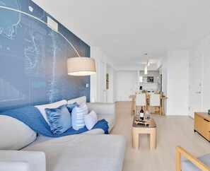 Ein modernes Wohnzimmer mit einer großen Wandkarte, einem Sofa mit blauen Kissen, einem Holztisch und einer Küche im Hintergrund.