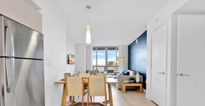 A modern kitchen with a stainless steel refrigerator, wooden dining table, and chairs. - Beachwalk 1BR with Stunning Intracoastal View (Hallandale Beach)
