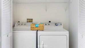 Een wasserijruimte met twee gestapelde wasmachines en drogers, een plank erboven en een mand op de droger.