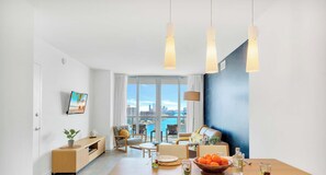 A modern living room with a city view, a dining area with a table set, and a seating arrangement. - Intracoastal View · 2BR Resort Suite & Balcony (Hallandale Beach)