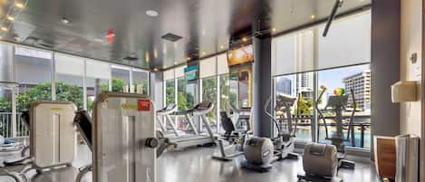 Ein Fitnessstudio mit Laufbändern, Kraftstationen und einem großen Fenster mit Blick auf die Stadt.