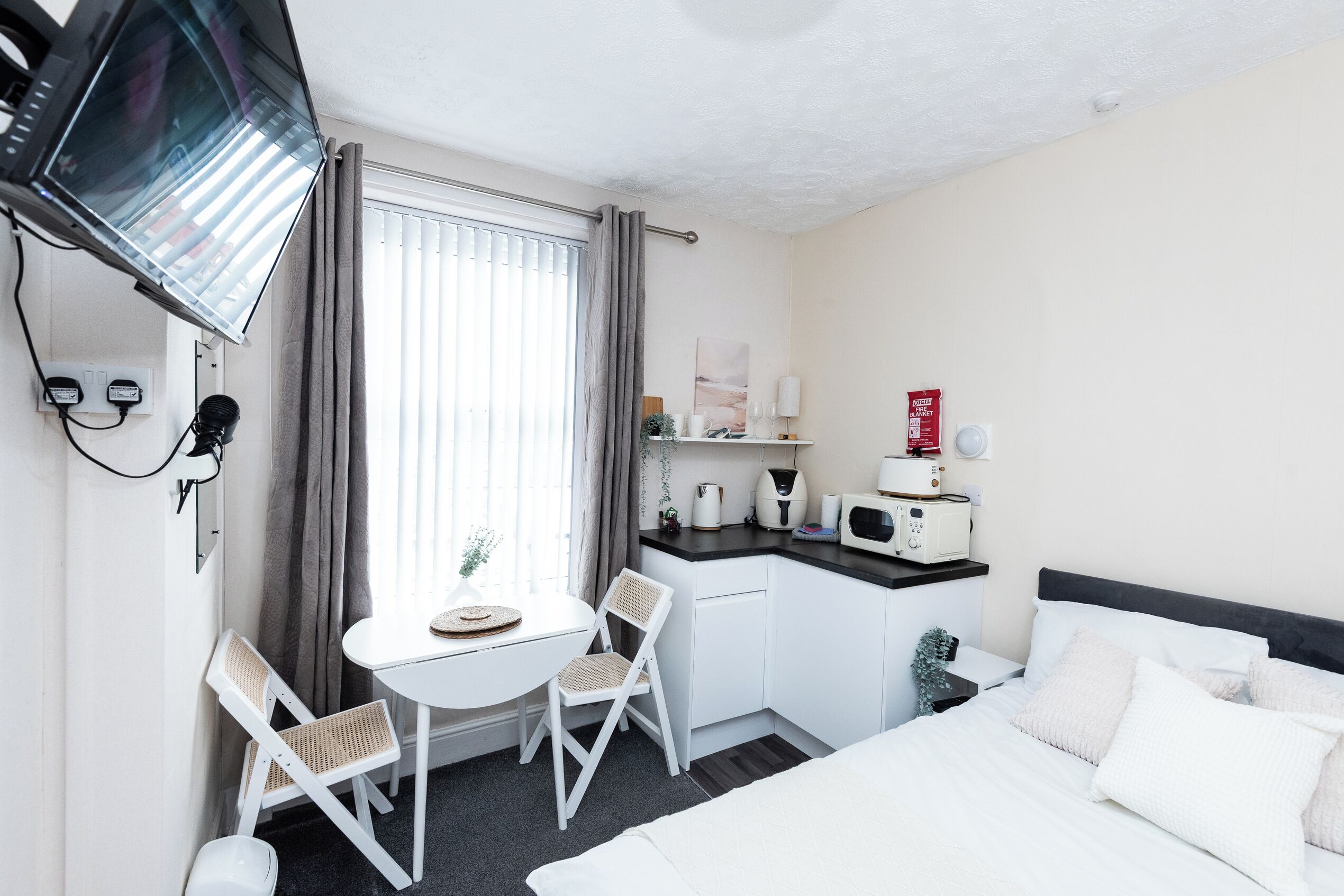 A hotel room with a bed, a desk with a chair, a television, and a window with curtains.