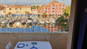 A view from a balcony with a table set for dining, overlooking a marina with boats and buildings in the background. - 2 rooms, with balcony overlooking the port (Leucate)