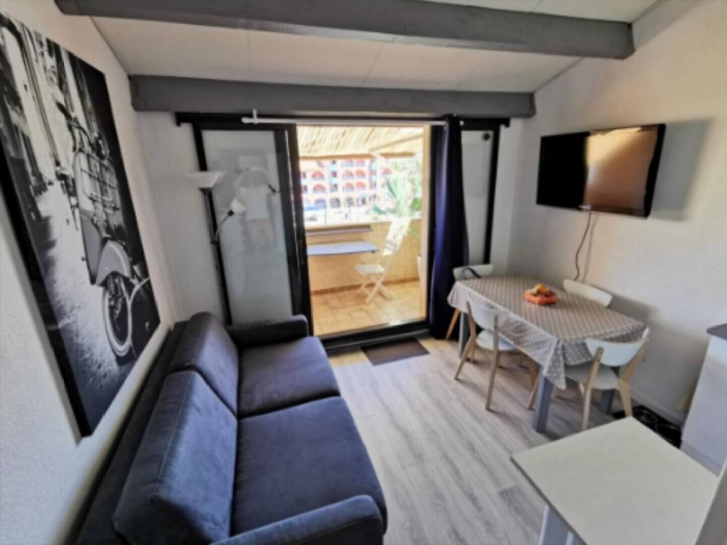 A compact room with a sofa, a small table, a TV, and a view through a glass door to an outdoor area.