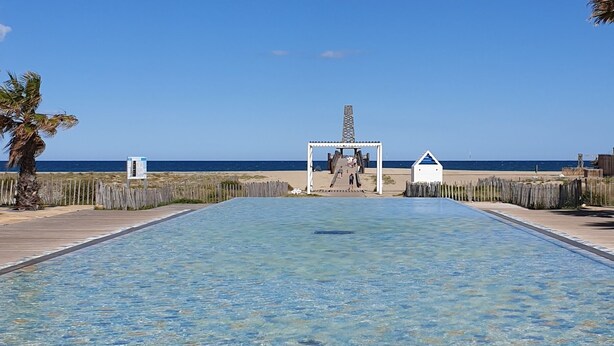 A clear blue sky, a swimming pool with a patterned floor, and a distant view of the ocean. - 2 rooms, with balcony overlooking the port (Leucate)
