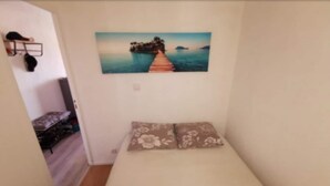 A small, narrow room with a bed, a painting of a pier and water, and a door leading to another room. - 2 rooms, with balcony overlooking the port (Leucate)