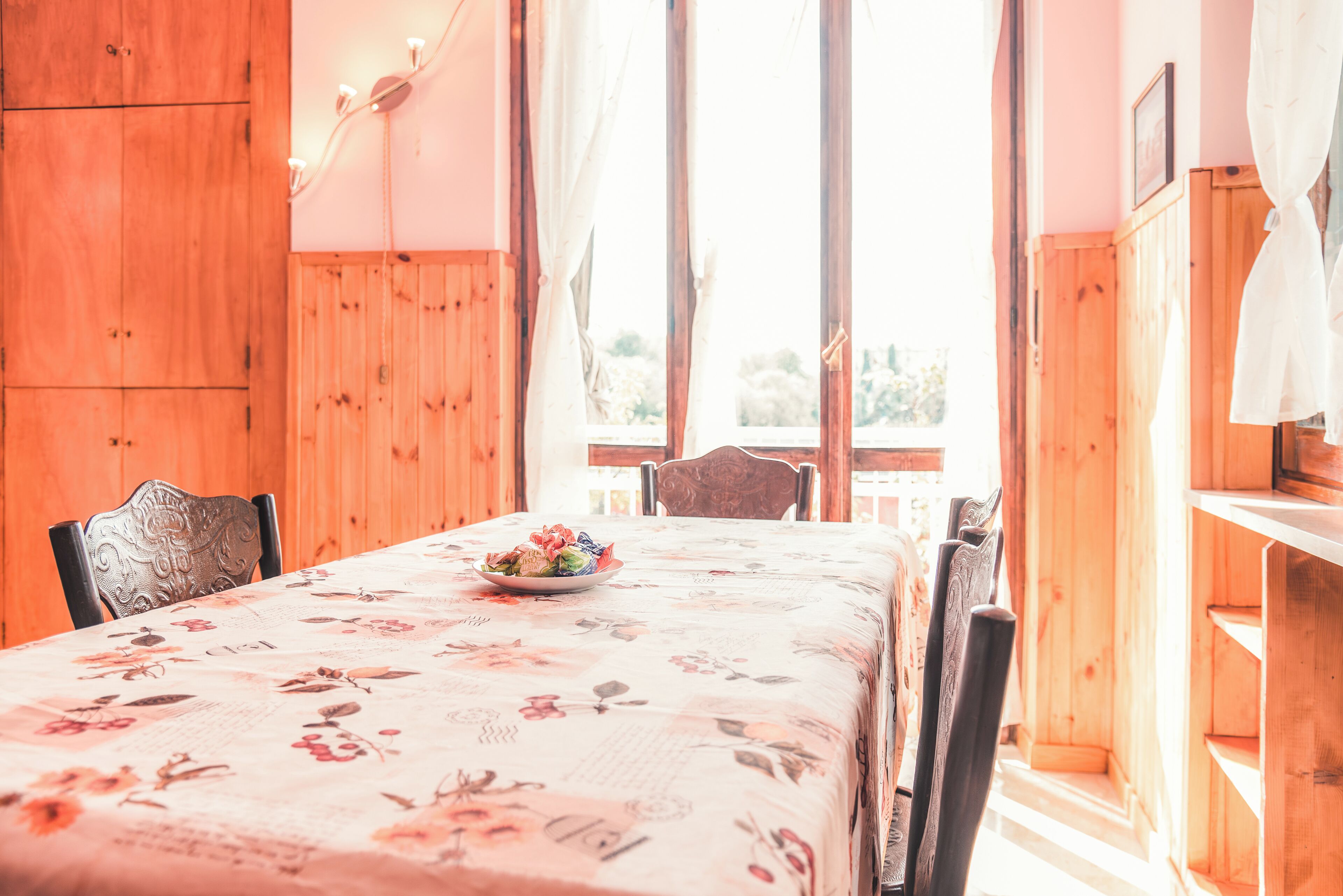 Una mesa de madera para comer con mantel floral, sillas y un cuenco de fruta.