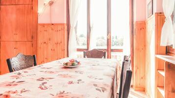 Una mesa de madera para comer con mantel floral, sillas y un cuenco de fruta.