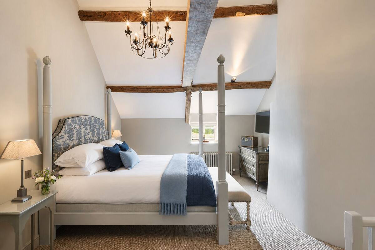 A bedroom with a four-poster bed, a chandelier, a dresser, and a window with a view.