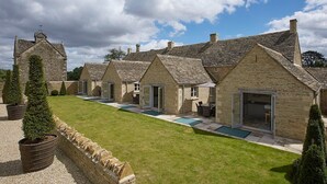 A row of stone cottages with individual doors and windows, a grassy lawn, and a clear sky.