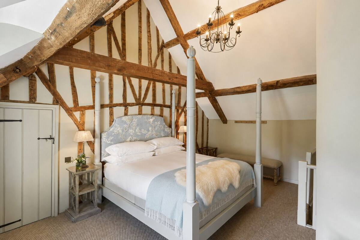 A bedroom with a four-poster bed, wooden beams, a chandelier, and a white door.