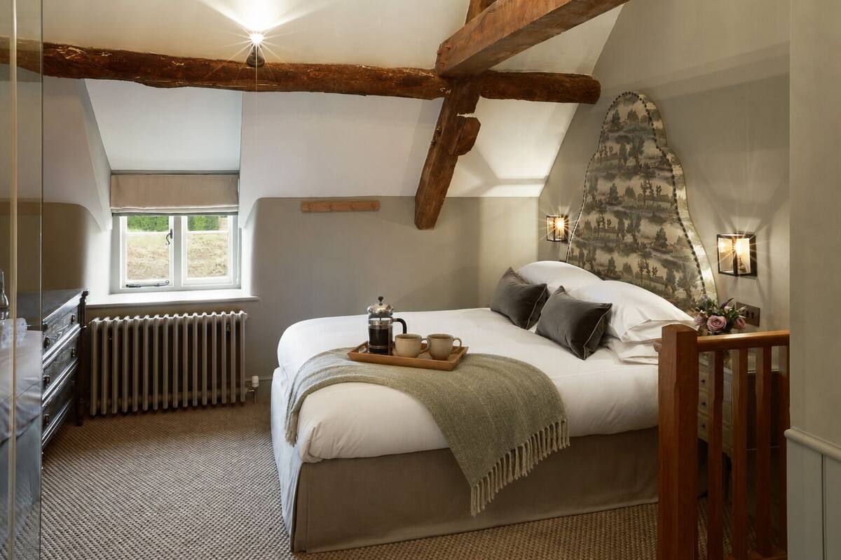A bedroom with a large bed, a radiator, a window, and a wooden ceiling beam.