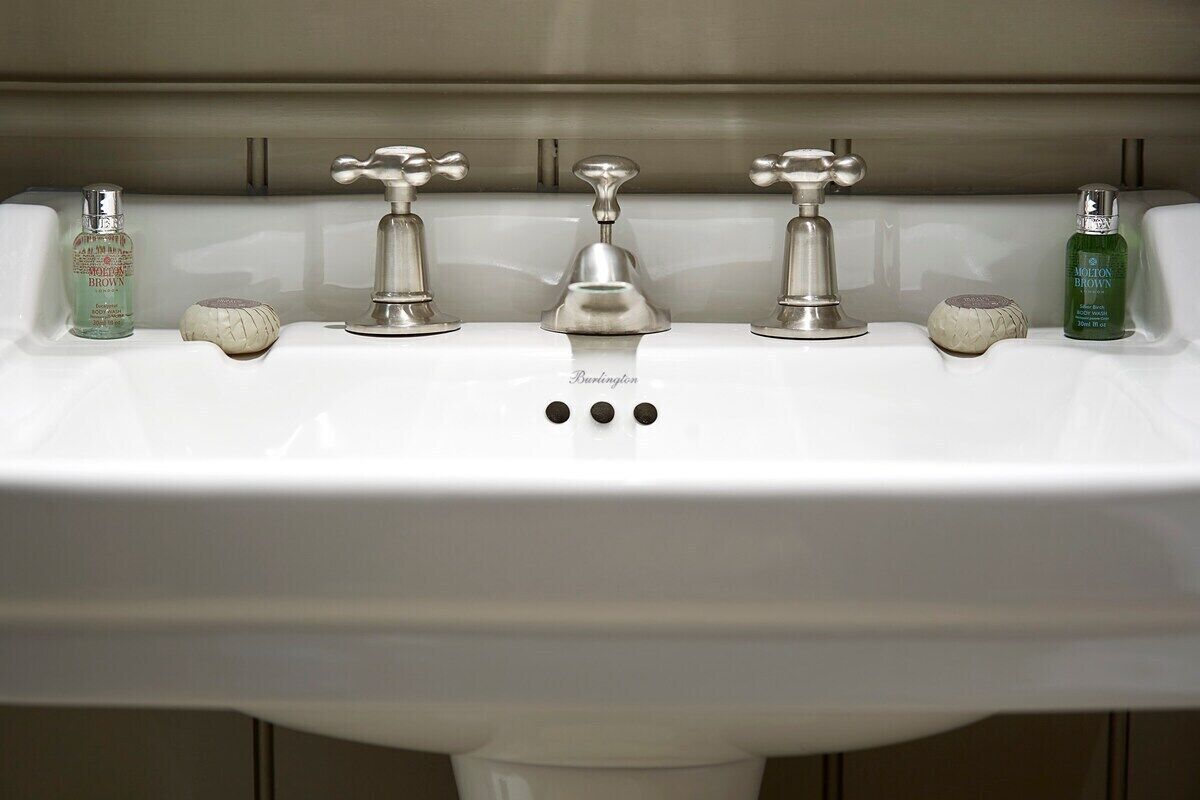 A bathroom sink with three faucets and two bottles of soap.