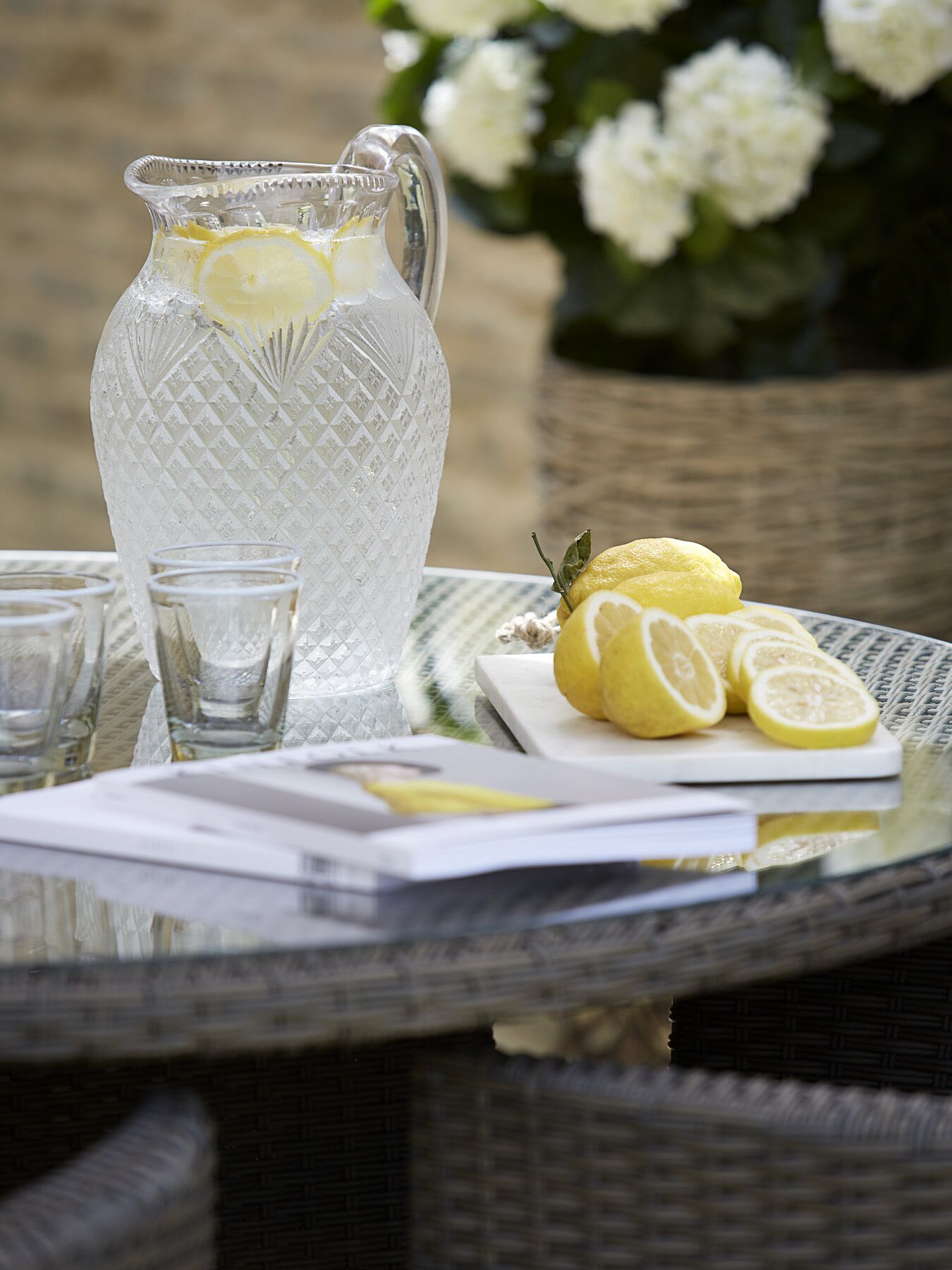 A clear glass pitcher with lemon slices, a plate with lemon slices, and glasses on a table.