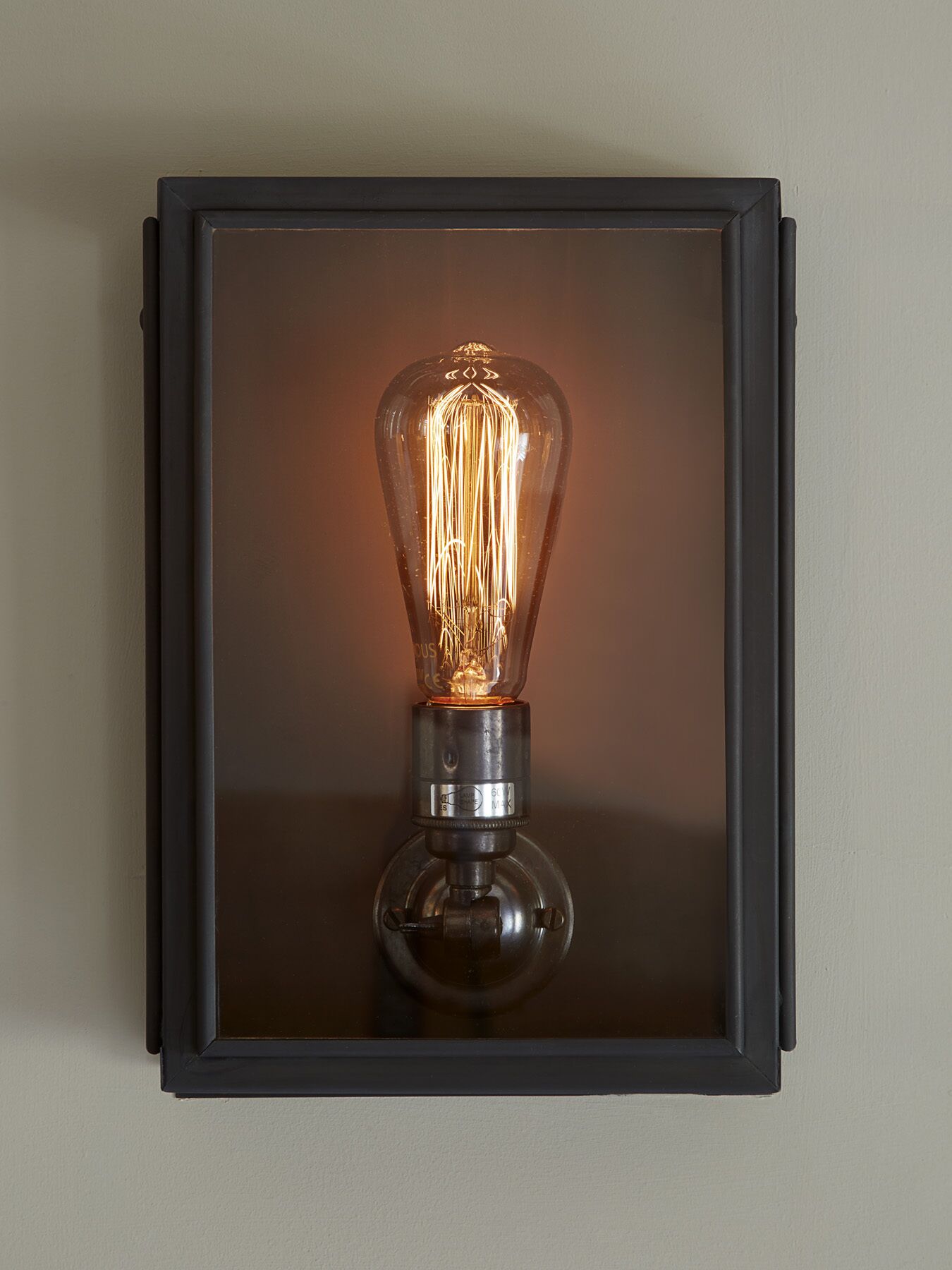 Un luminaire mural doté d’un abat-jour en verre transparent et d’un socle en métal.