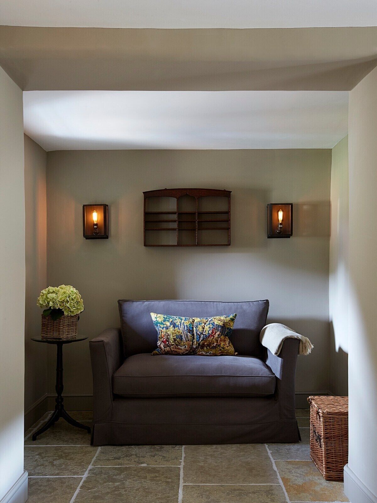 A cozy corner with a dark brown sofa, a colorful pillow, and two wall-mounted sconces.