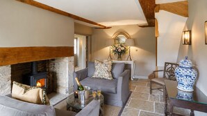 A cozy living room with a stone fireplace, a grey sofa, a glass coffee table with a bottle and glasses, and a blue and white vase.