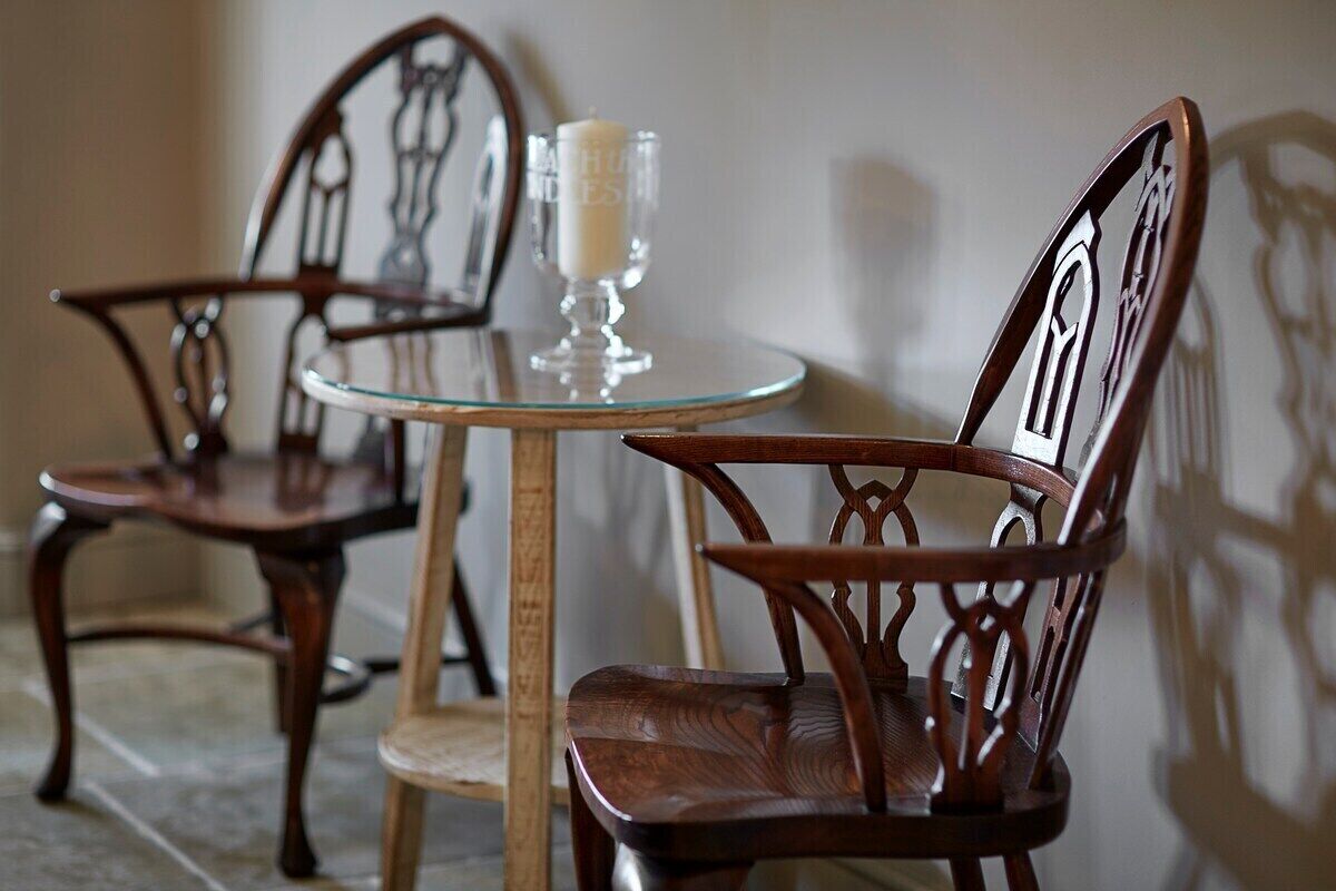 Two wooden chairs with intricate back designs, a small round glass table, and a candle on the table.
