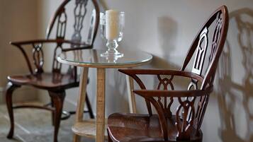 Two wooden chairs with intricate back designs, a small round glass table, and a candle on the table.